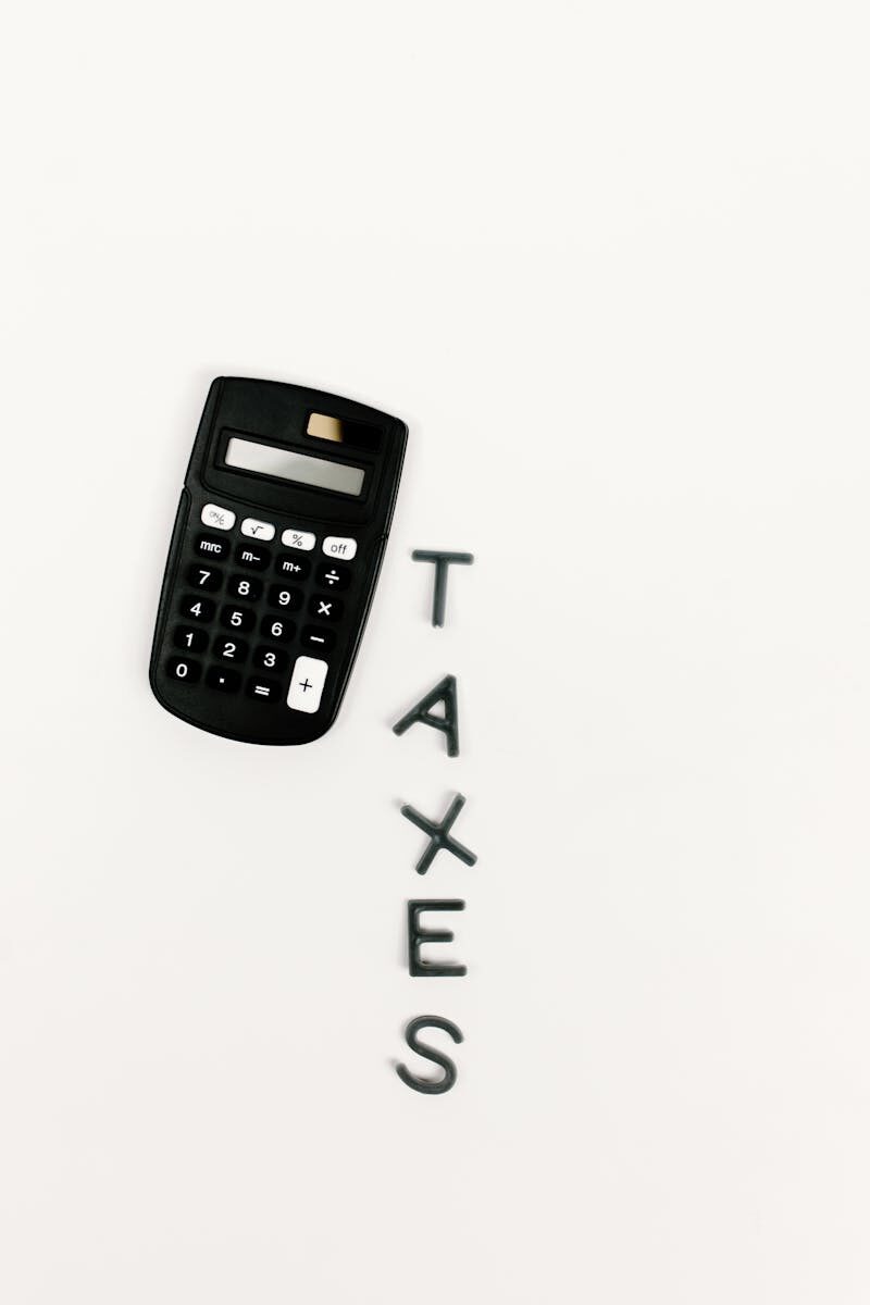 Black calculator and letter tiles spelling 'TAXES' on a smooth white background, symbolizing financial calculations.